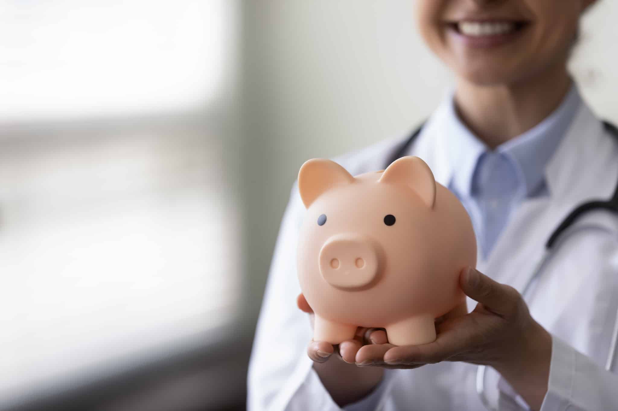Close up of a medical professional holding a piggy bank