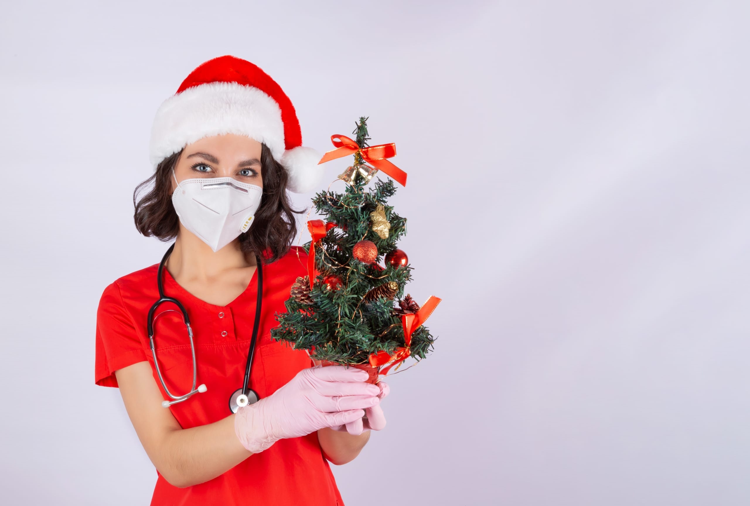 Nurse in a Santa hat holding a miniature Christmas tree