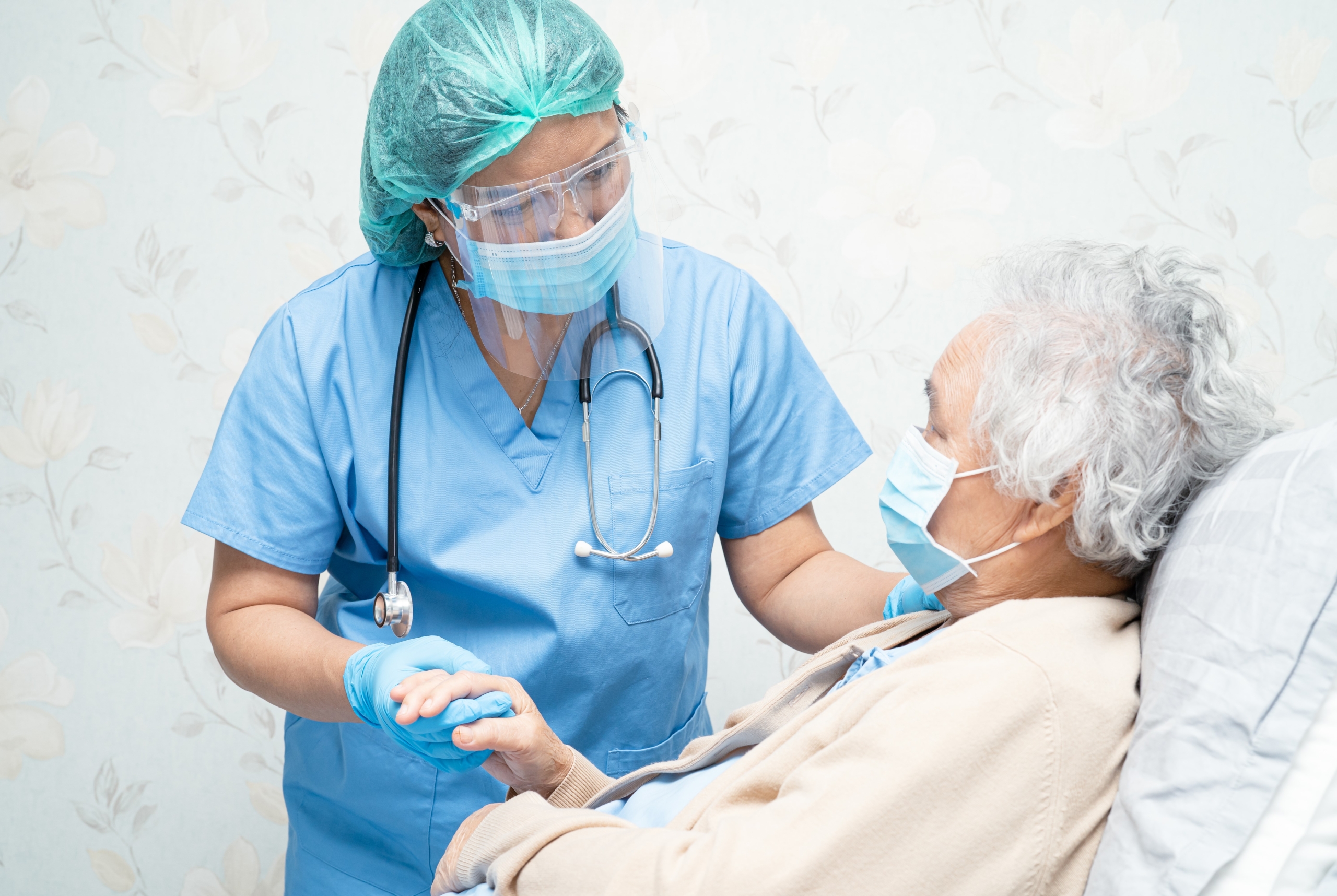 Nurse in PPE gear holding the hand of an elderly patient