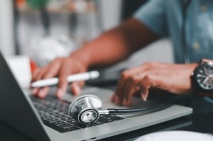 Close up of a male nurse with a stethoscope using a laptop