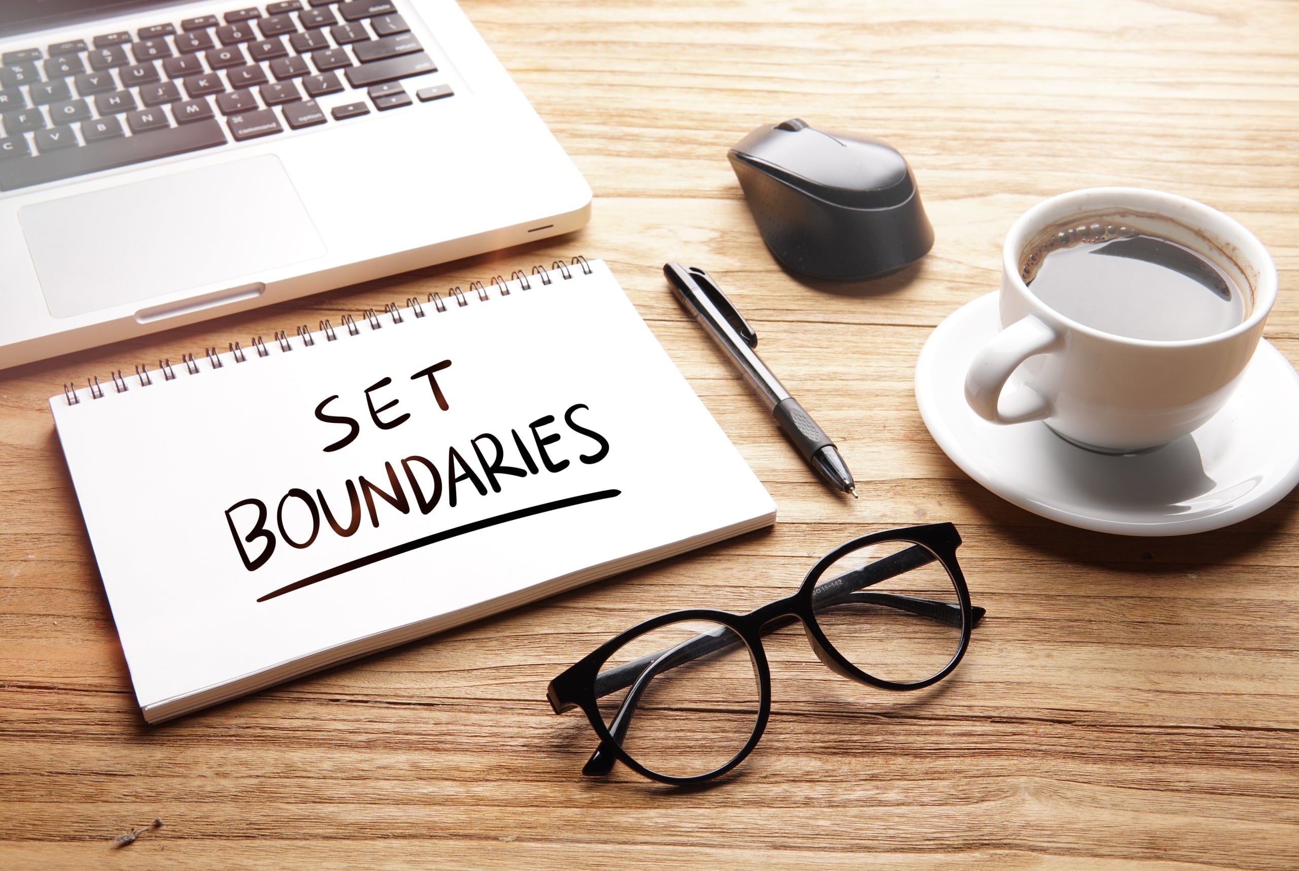 A notebook that says set boundaries next to a cup of coffee and glasses