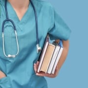 Nursing student in blue scrubs with a stack of books