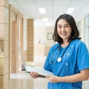 Asian nurse smiling with paperwork in a hospital hallway