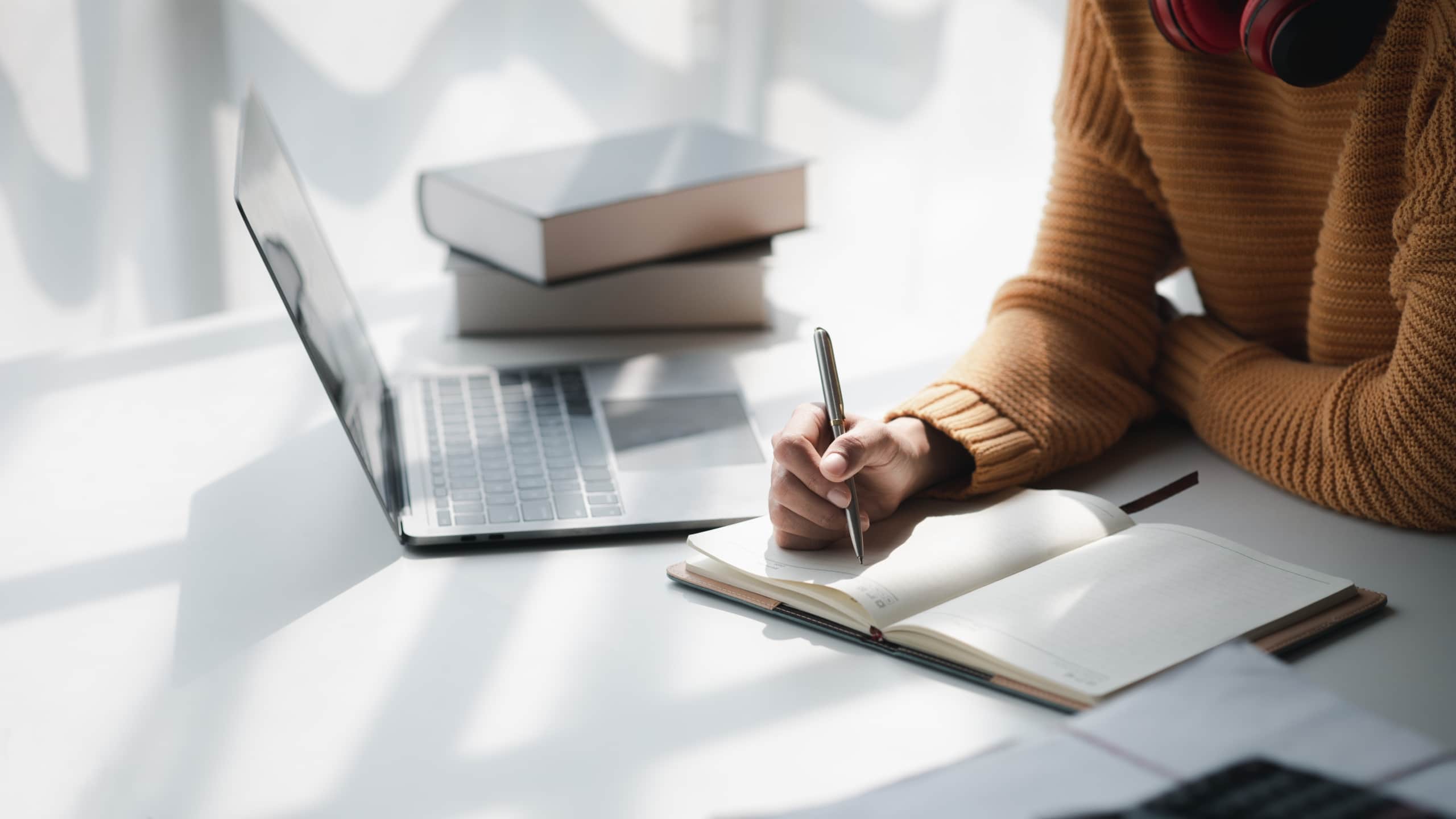 Close up of a woman taking notes while using a laptop
