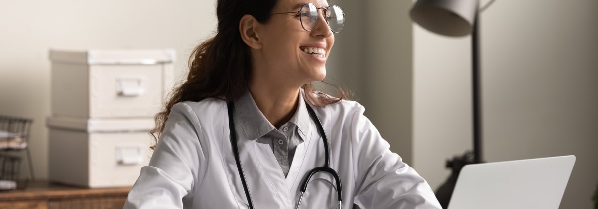 Young medical professional smiling and using a laptop