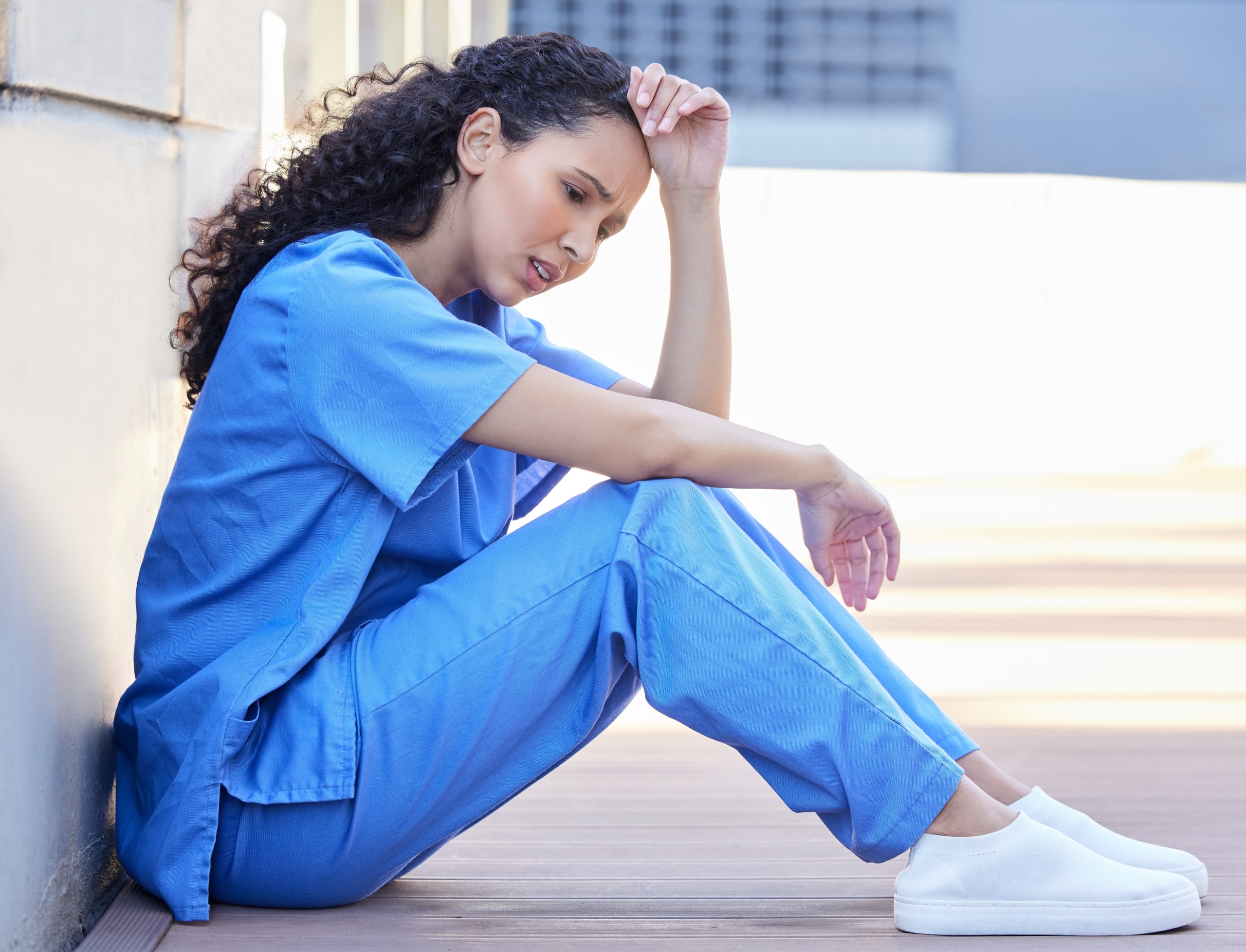 Stressed nurse sitting outside against a wall